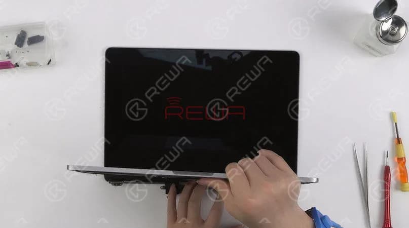 Una vez hecho esto, instale la barra de resorte. Apriete los tornillos que fijan la barra de hierro de la pantalla y luego consiga la tira del LOGO adherida. Ensamble la pantalla y la mitad inferior del teclado. Continúe con la instalación de la antena WiFi y la fijación del cable flexible de la pantalla. Apriete los tornillos que fijan la antena WiFi y la pantalla. Una vez terminado, conecte la batería e instale la carcasa inferior. 