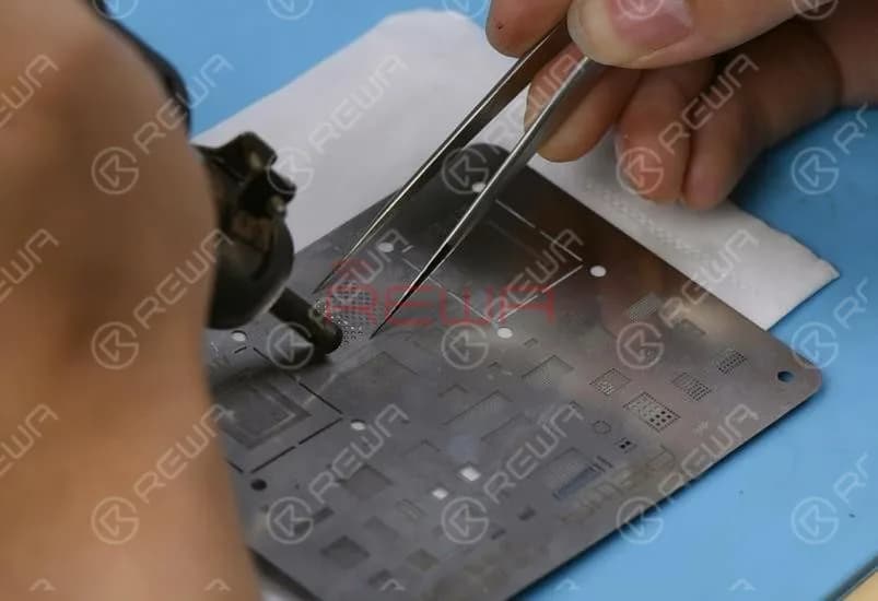 Als Nächstes müssen wir den NAND-Flash-Chip neu kugeln (reballen). Richten Sie die BGA-Reballing-Schablone genau am Chip aus. Tragen Sie Lötzuspast gleichmäßig auf die BGA-Reballing-Schablone auf und erhitzen Sie sie dann gleichmäßig mit der QUICK 990AD Heißluftpistole, damit alle Lötkugeln vollständig aushärten können.